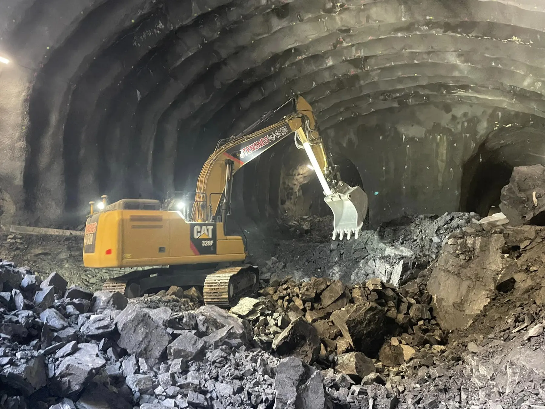 Gravemaskin i arbeid inne i fjelltunnel